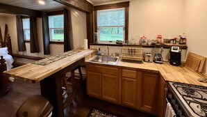 A kitchen with a wooden island, a sink, a stove, and a window with a view of greenery.