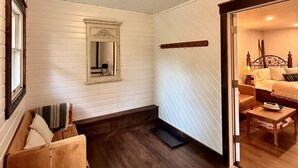 A room with white paneled walls, a wooden bench, a mirror, and a bed with a headboard.