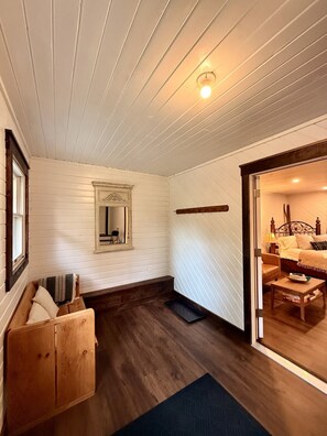 A room with white paneled walls, a wooden bench, a mirror, and a bed with a headboard.
