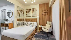 A modern bedroom with a large bed, a wooden headboard, a round mirror, and a wall clock. - Inspiria Fully-Furnished Studio with Balcony (NEW) (Davao City)