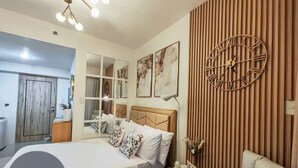 A modern bedroom with a large bed, a clock on the wall, and a view of the bathroom. - Inspiria Fully-Furnished Studio with Balcony (NEW) (Davao City)