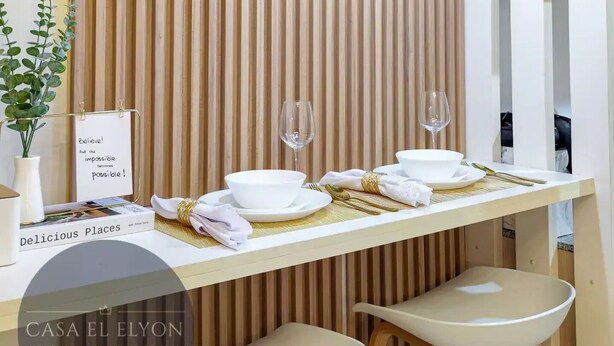 A dining area with a wooden slat wall, pendant lights, a table set with white plates, glasses, and cutlery, and a sign that reads "Believe! And the impossible becomes possible!" - Inspiria Fully-Furnished Studio with Balcony (NEW) (Davao City)