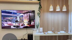 A modern living room with a large TV displaying a festive scene, a cozy seating area, and a dining setup with a menu. - Inspiria Fully-Furnished Studio with Balcony (NEW) (Davao City)