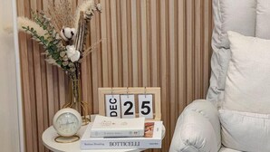 A corner of a room with a striped wall, a white chair, a small table with a clock, a vase with dried plants, and a calendar displaying December 25. - Inspiria Fully-Furnished Studio with Balcony (NEW) (Davao City)
