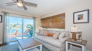 A living room with a sofa, two side tables, a coffee table, a ceiling fan, a large window with blinds, and a framed picture on the wall. - Relax and Unwind at Beautiful Bahia Palms (Indian Rocks)