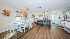 A spacious kitchen with white cabinetry, a dining area with white chairs, and a bar area with stools. - Relax and Unwind at Beautiful Bahia Palms (Indian Rocks)