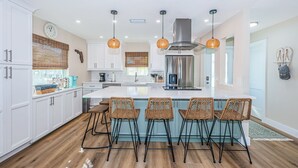 A modern kitchen with white cabinets, a stainless steel refrigerator, and a central island with bar stools. - Relax and Unwind at Beautiful Bahia Palms (Indian Rocks)