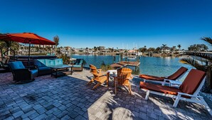 A waterfront patio with outdoor seating, a red umbrella, and a view of the marina and buildings in the background. - Relax and Unwind at Beautiful Bahia Palms (Indian Rocks)