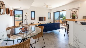 Ein modernes Wohnzimmer mit einem Glastisch, Korbstühlen, einem blauen Sofa und einem Balkon mit Aussicht.