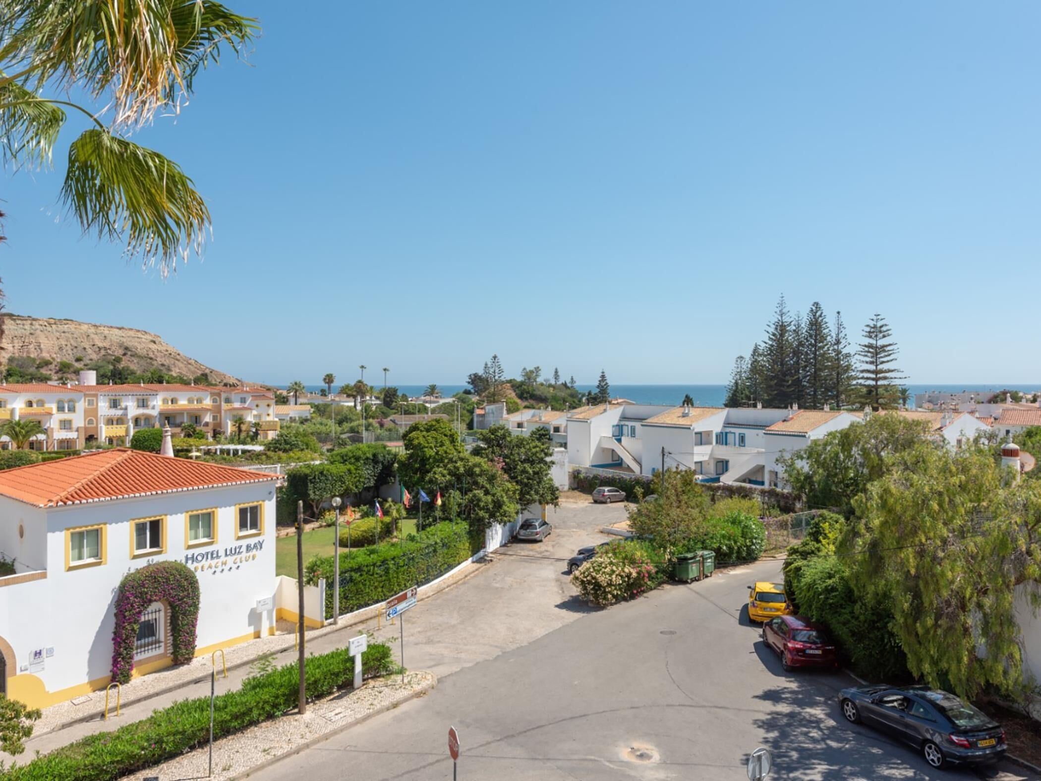 Un hotel frente al mar con vistas a la playa, varias construcciones y coches aparcados.