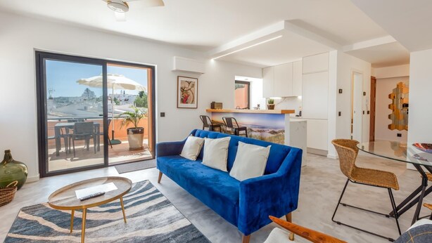 Ein modernes Wohnzimmer mit einem blauen Sofa, einem Glastisch und Blick auf die Stadt durch eine Schiebetür.