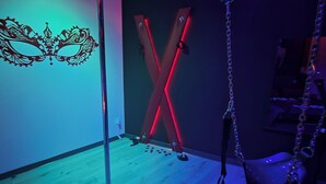 A room with a wooden floor, a wall-mounted decorative mask, and red lighting fixtures. - L'escale du Desir Love Room spa Privatif (Calais)