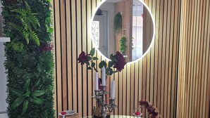 A room with a round mirror, two white vases with red flowers, a small table with a red mat, and a vertical plant wall. - L'escale du Desir Love Room spa Privatif (Calais)