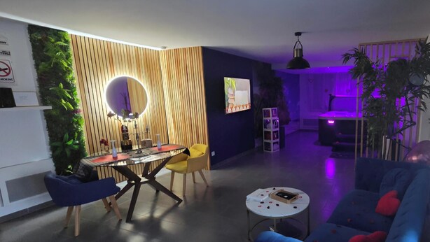 A modern living room with a round mirror, a dining table, a sofa, and a TV. - L'escale du Desir Love Room spa Privatif (Calais)
