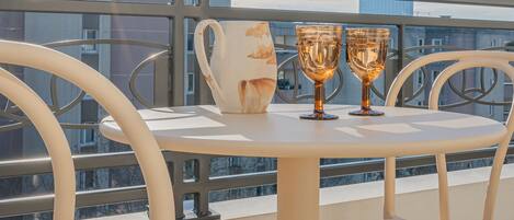 A round table with two glasses and a pitcher on a balcony with metal railings and city views.