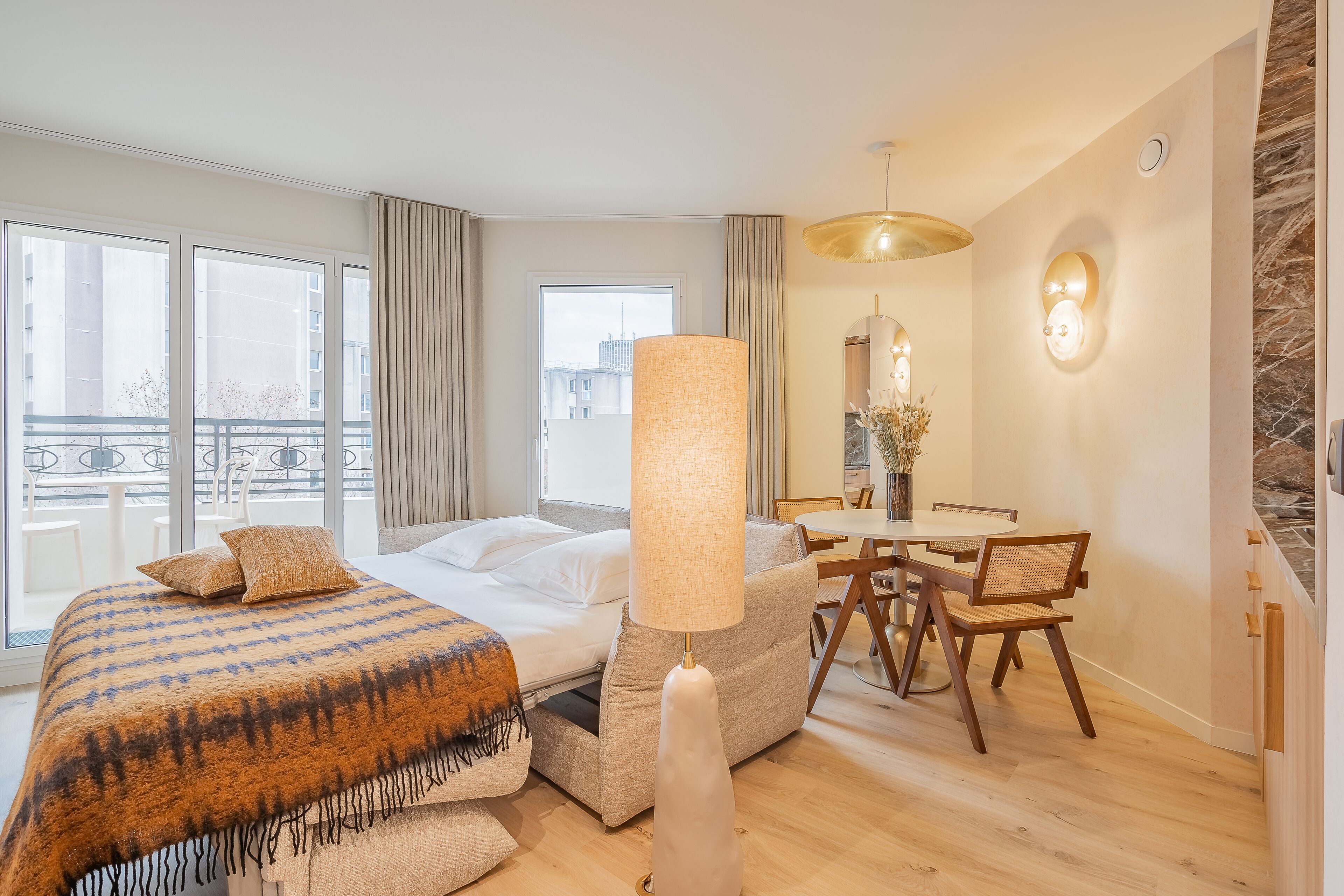 Een hotelkamer met een bed, een zithoek met een tafel en stoelen, een groot raam en een balkon.