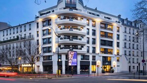 A multi-story hotel with a curved facade, balconies, and illuminated signage. - Yuna Porte Maillot - ApartHotel (Paris)