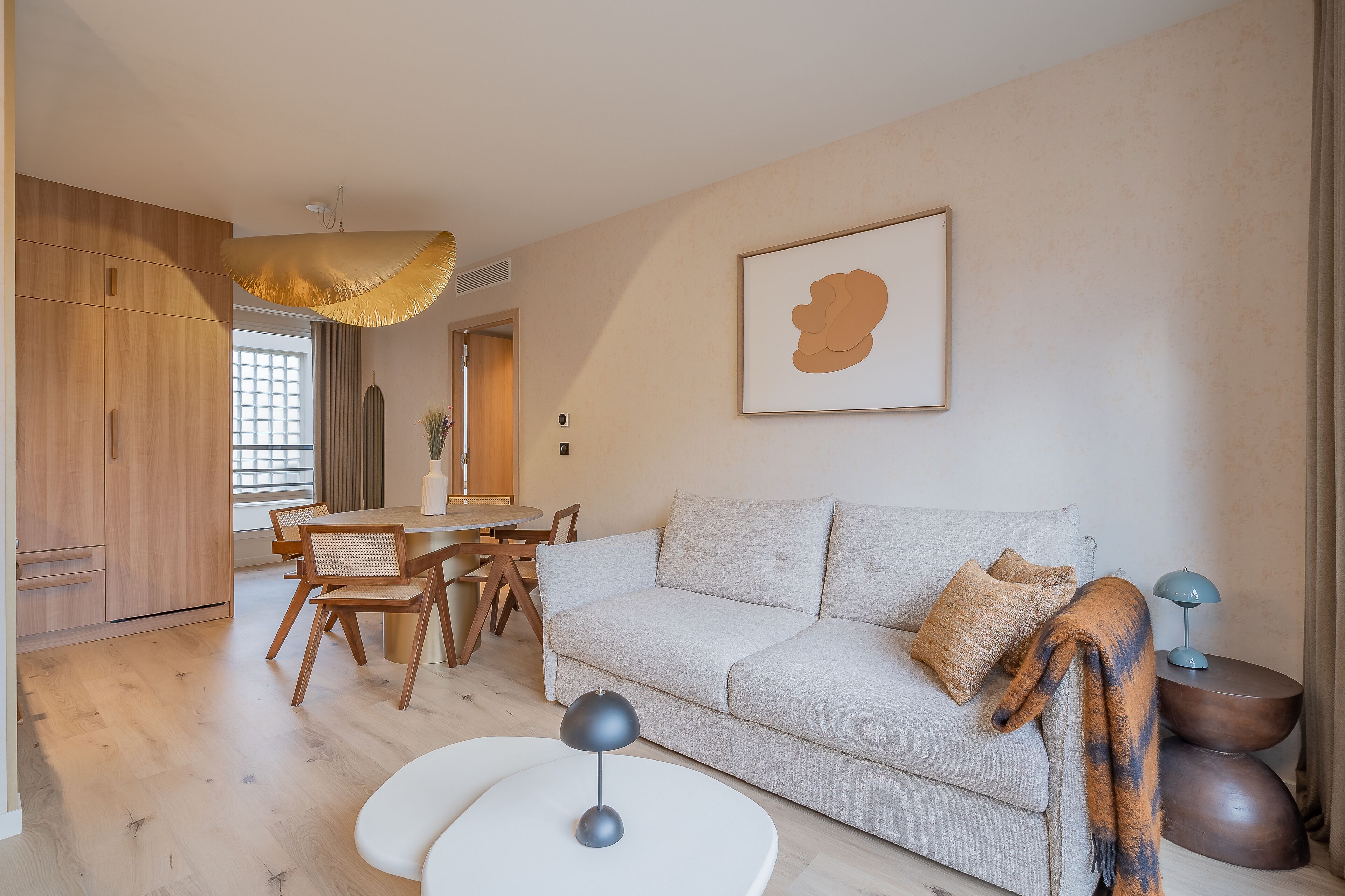 Ein modernes Wohnzimmer mit einer Couch, einem Esstisch mit Stühlen, einer Pendelleuchte und einem gerahmten Kunstwerk an der Wand.