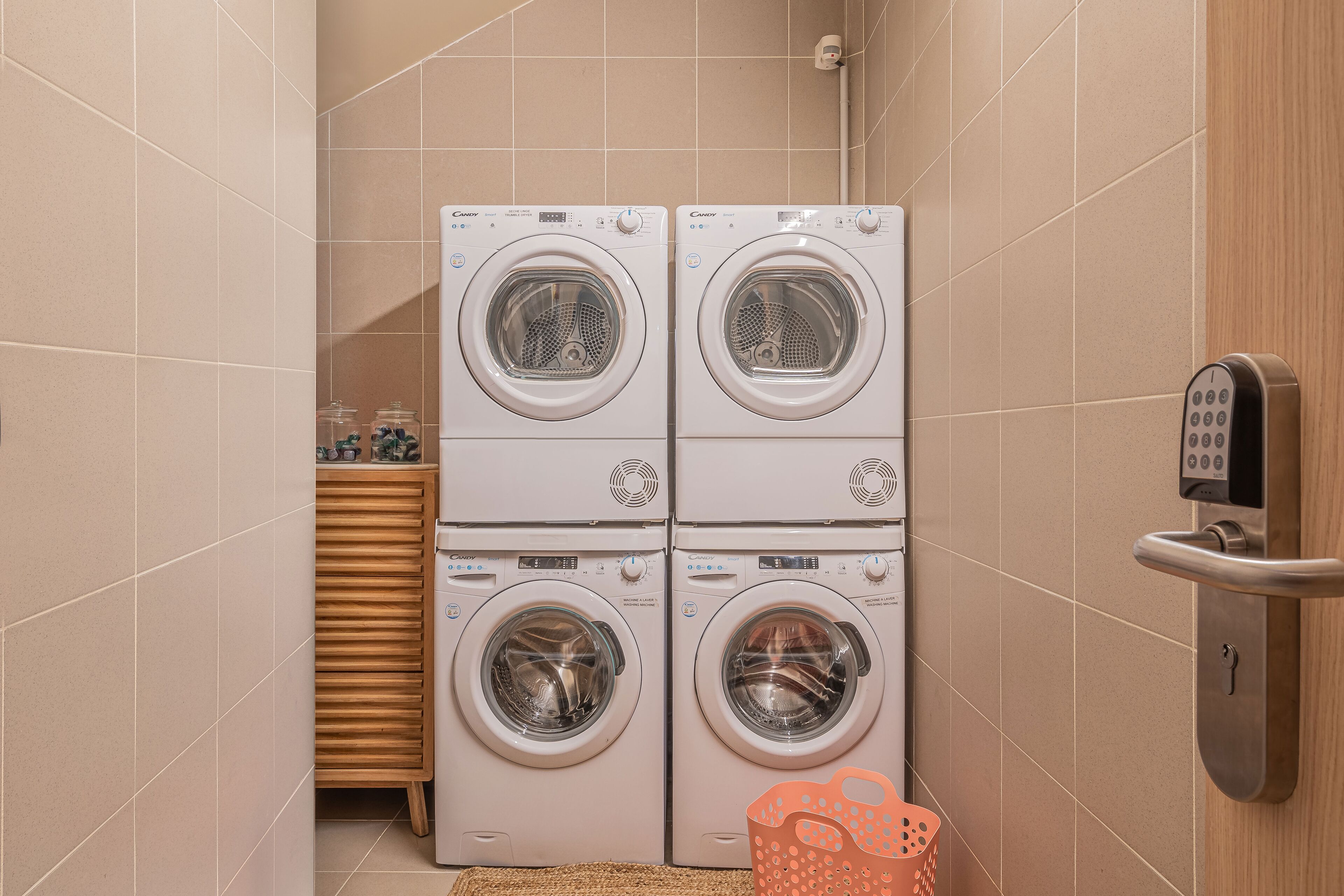 A laundry room with four stacked front-loading washing machines, a wooden cabinet, and a wall-mounted electronic lock.