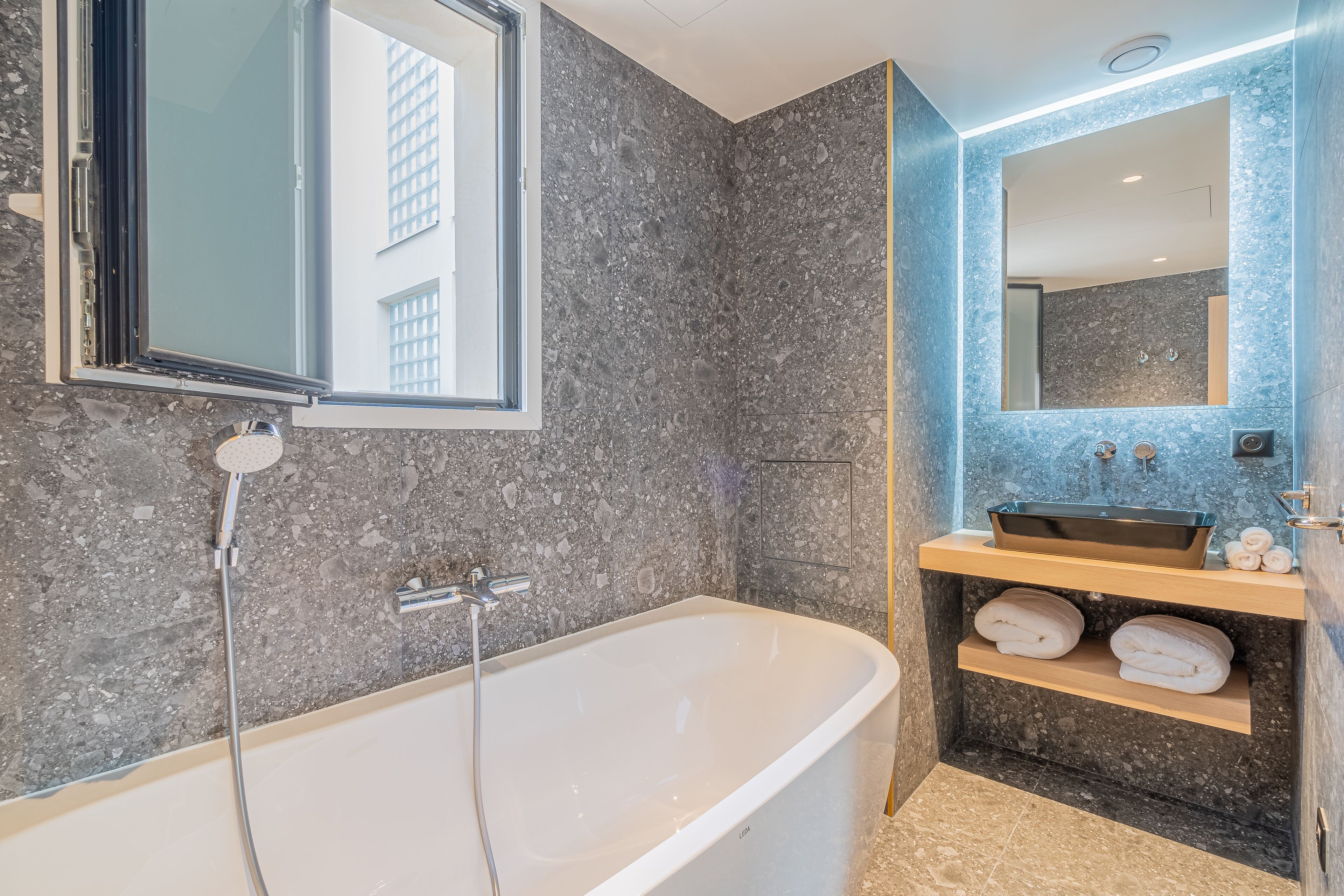 Een moderne badkamer met een vrijstaand bad, een grote spiegel en een inbouwspoelbak met een marmeren aanrechtblad.