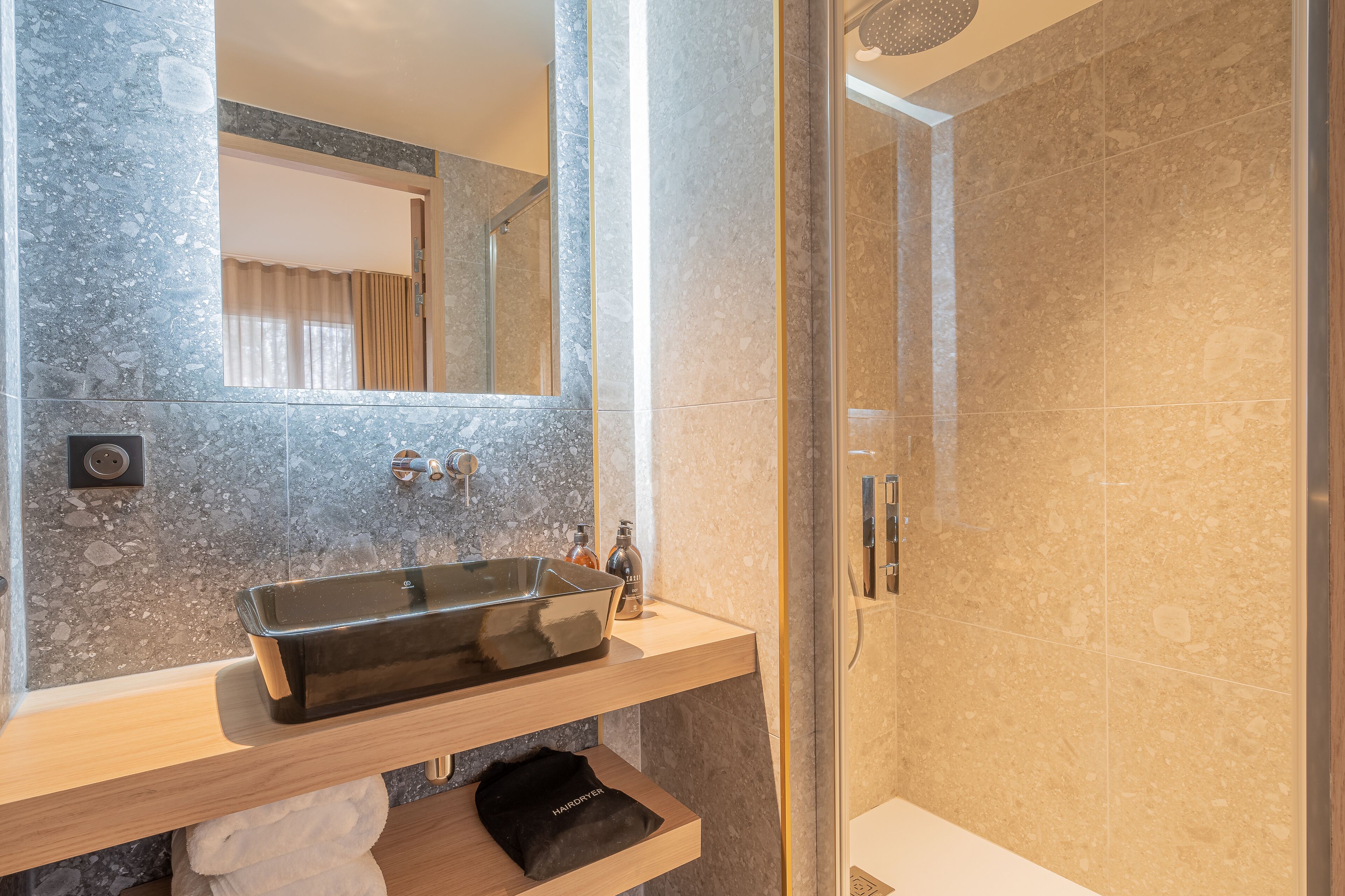 A modern bathroom with a marble sink, a mirror, and a shower enclosure.