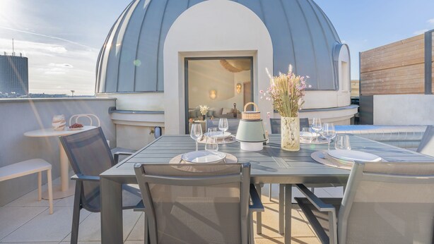 An outdoor dining area with a table set for two, a large dome structure, and a view of the city skyline. - Yuna Porte Maillot - ApartHotel (Paris)