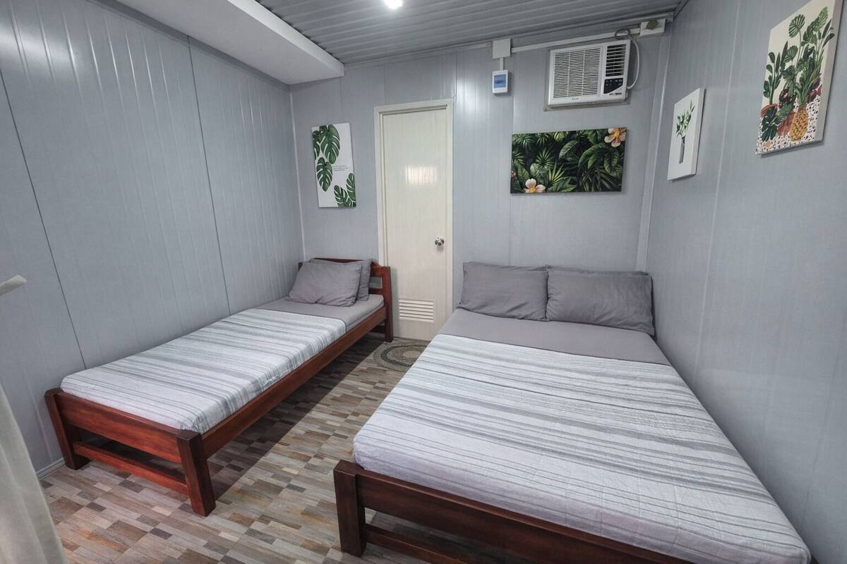 A room with two single beds, a door, and wall-mounted air conditioning units.