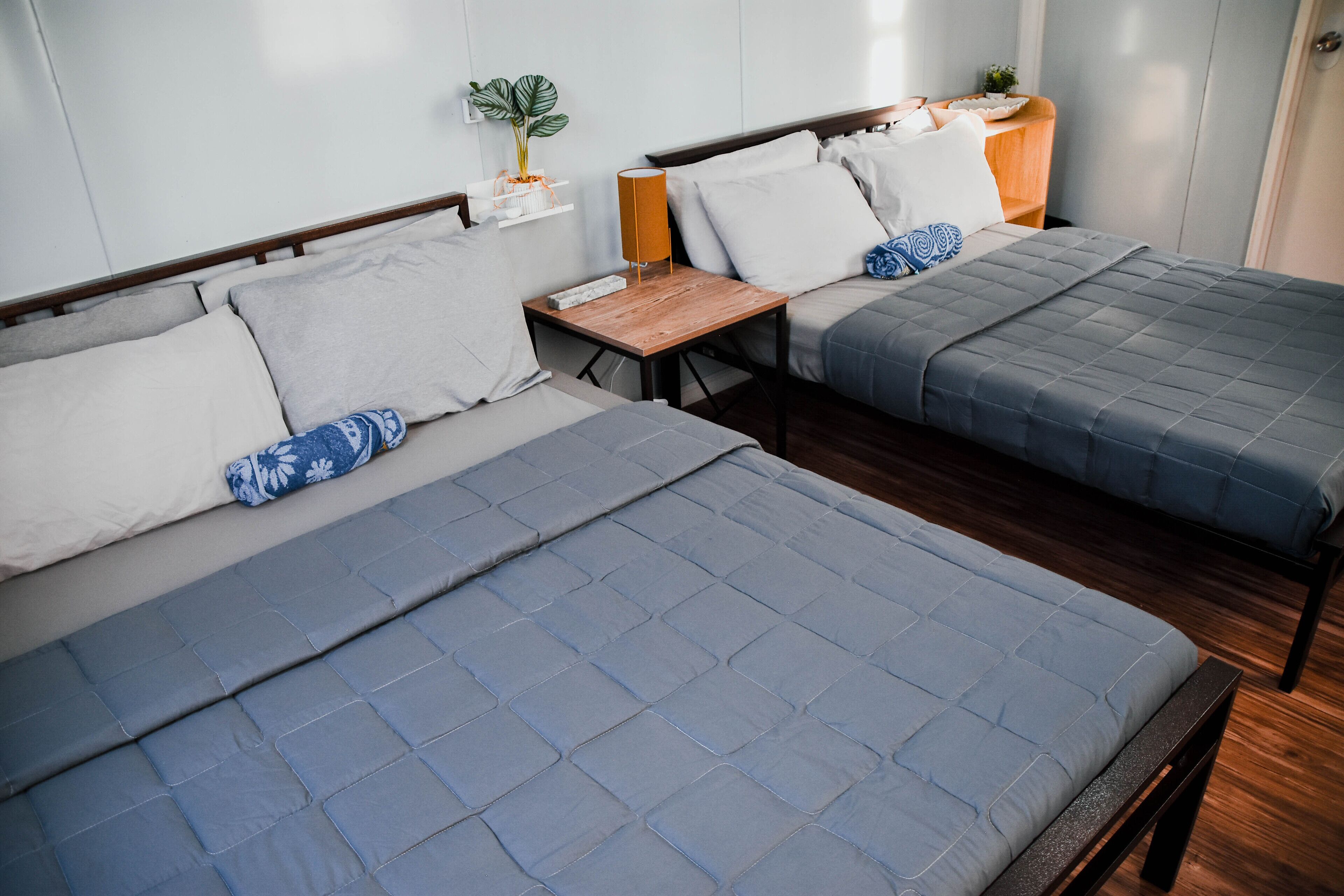 Two beds with grey bedding, wooden headboards, and bedside tables with lamps.