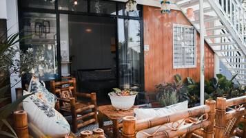 An outdoor seating area with bamboo furniture, a potted plant, and a staircase leading to an upper level.