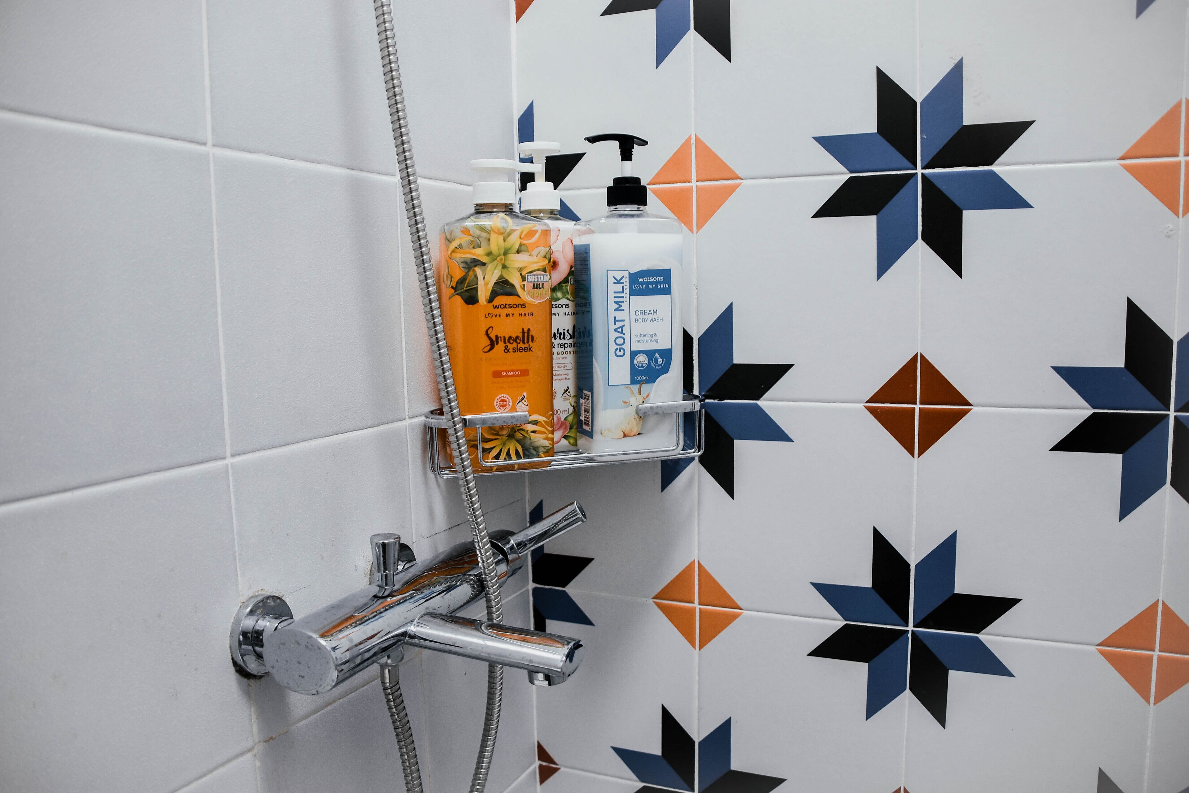 Un baño con ducha, dispensador de jabón y una botella de loción sobre una repisa.