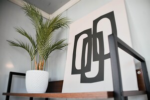 Una maceta blanca con textura y una planta sobre un estante de madera, junto a una gran obra de arte abstracta en blanco y negro.