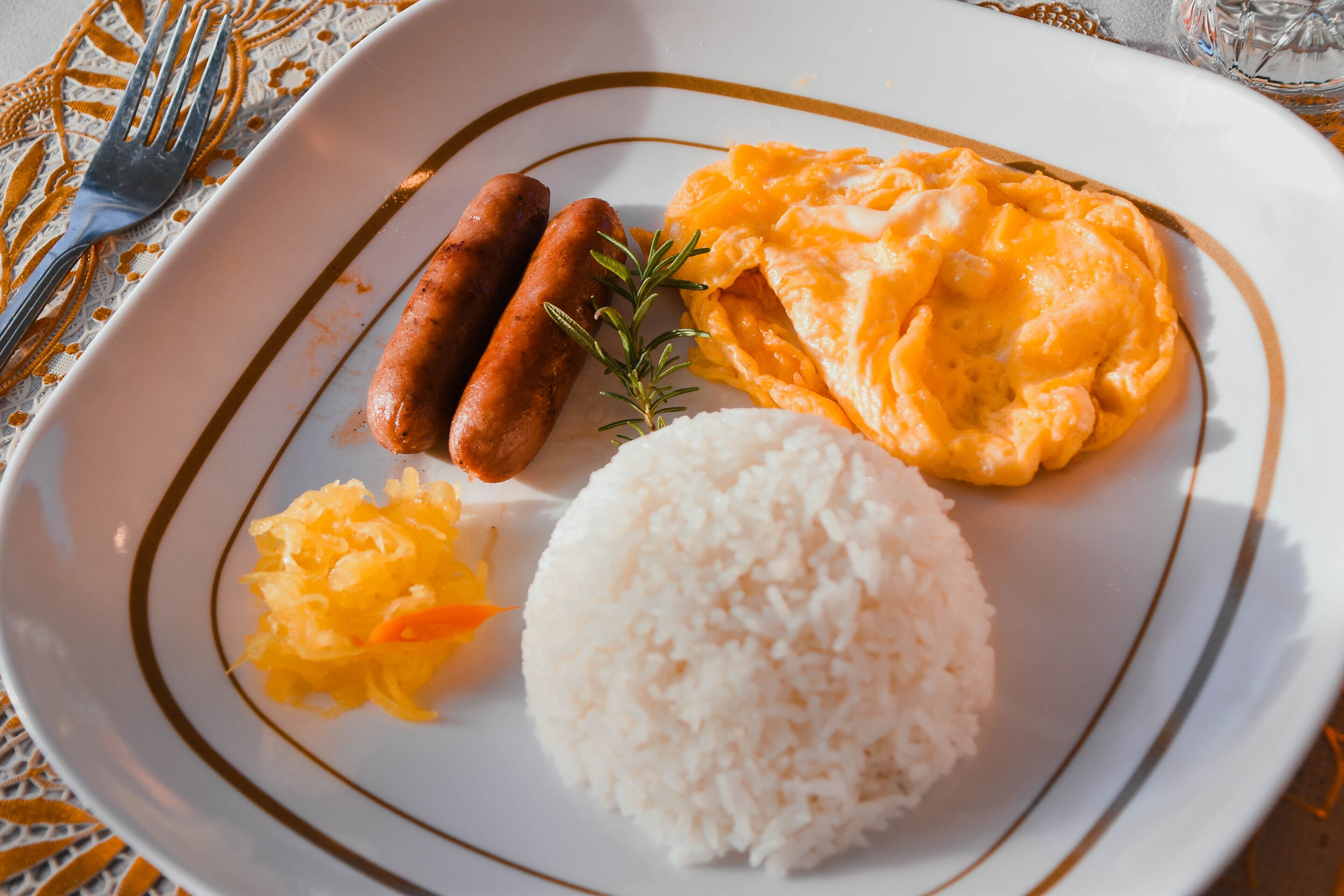 A plate with white rice, scrambled eggs, sausages, and sauerkraut.