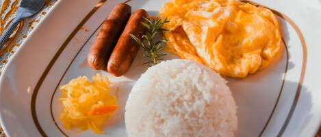 A plate with white rice, scrambled eggs, sausages, and sauerkraut.