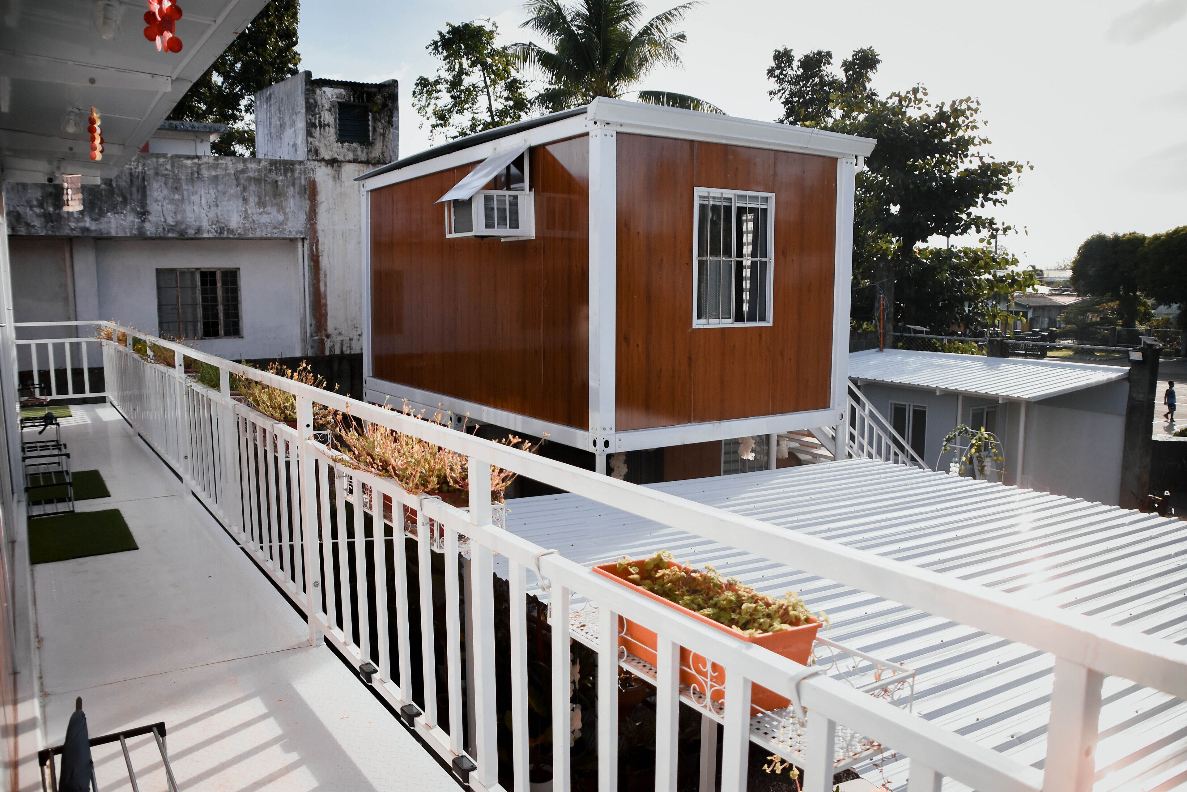 Un bâtiment moderne avec une façade en bois et des balustrades blanches, doté d’un balcon agrémenté de plantes en pot.