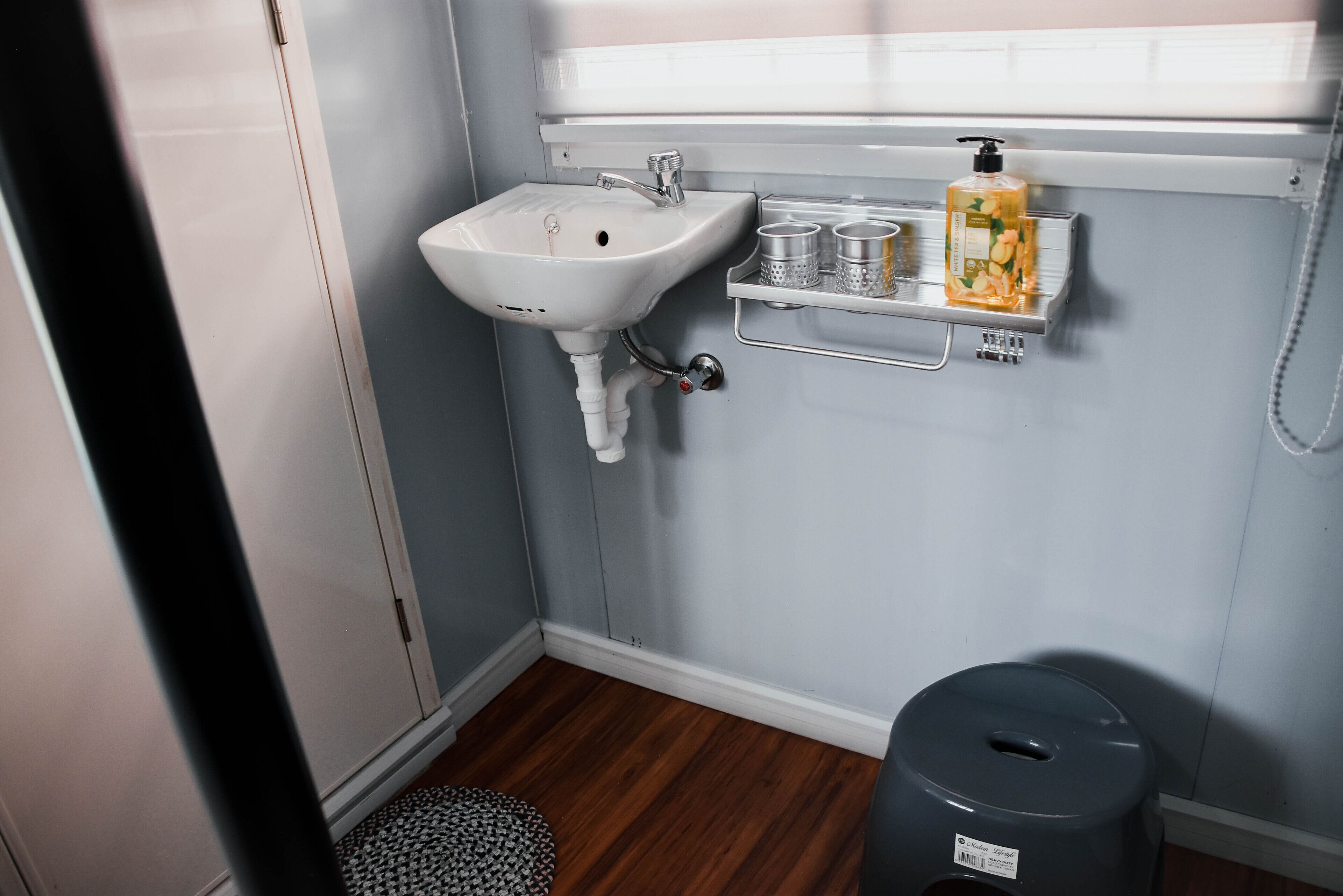 Une salle de bain avec un lavabo blanc, une petite étagère contenant des articles de toilette et une poubelle grise.