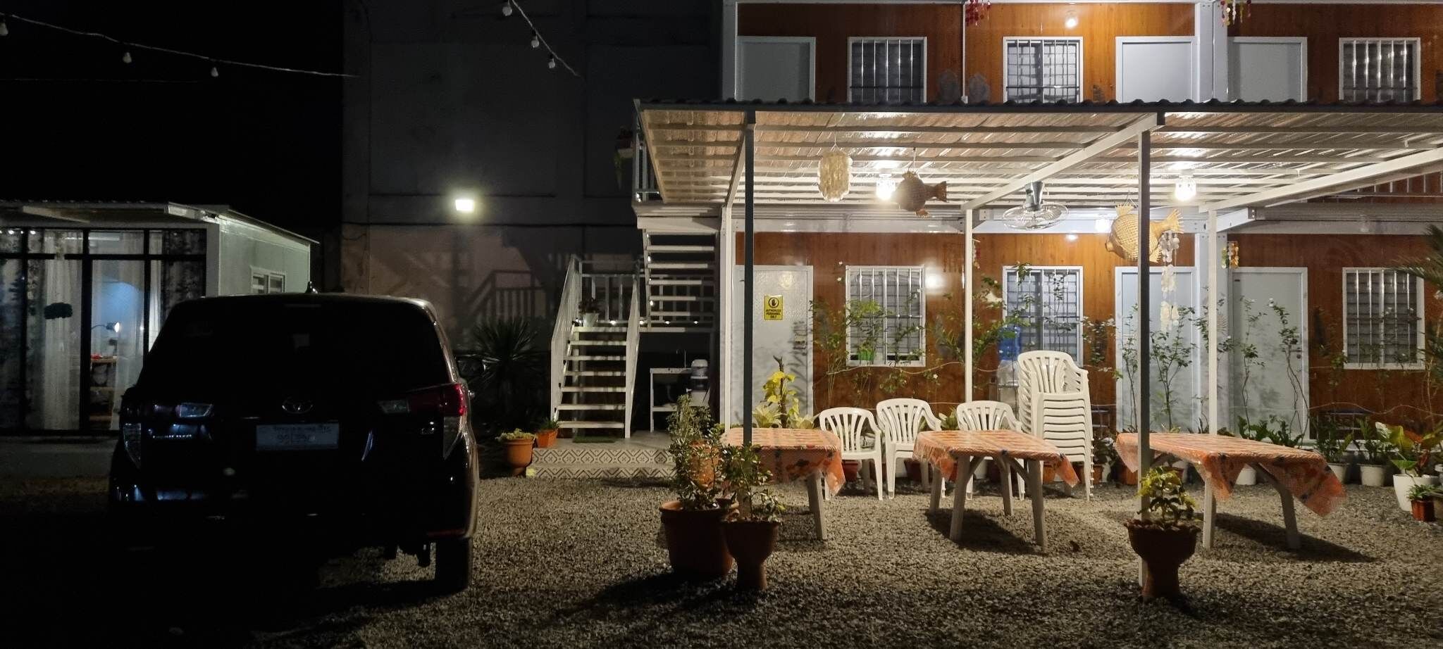 A covered outdoor seating area with tables and chairs, surrounded by potted plants.