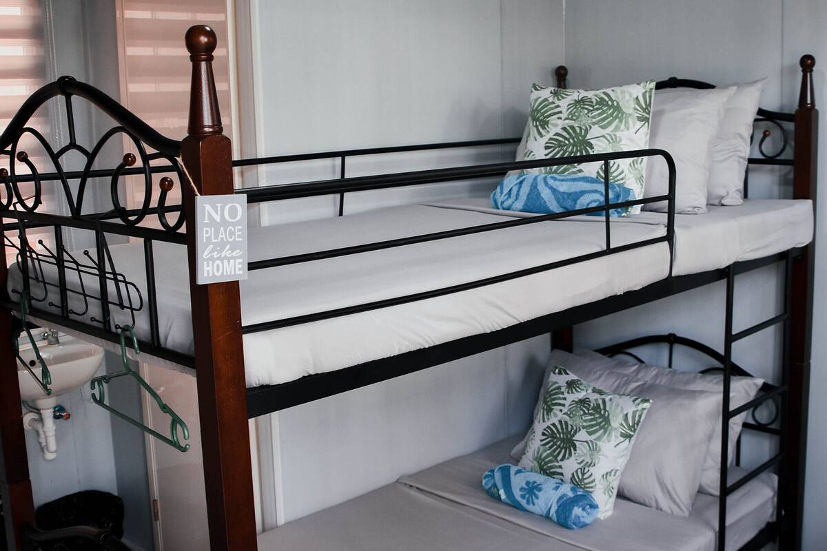 A bunk bed with a "NO PLACE like HOME" sign, wooden headboard, and white bedding.