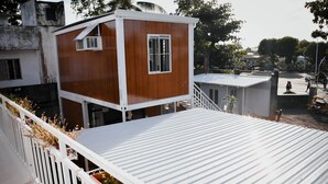 Una pequeña cabaña de madera con fachada blanca, un balcón con barandilla blanca y un techo de metal.