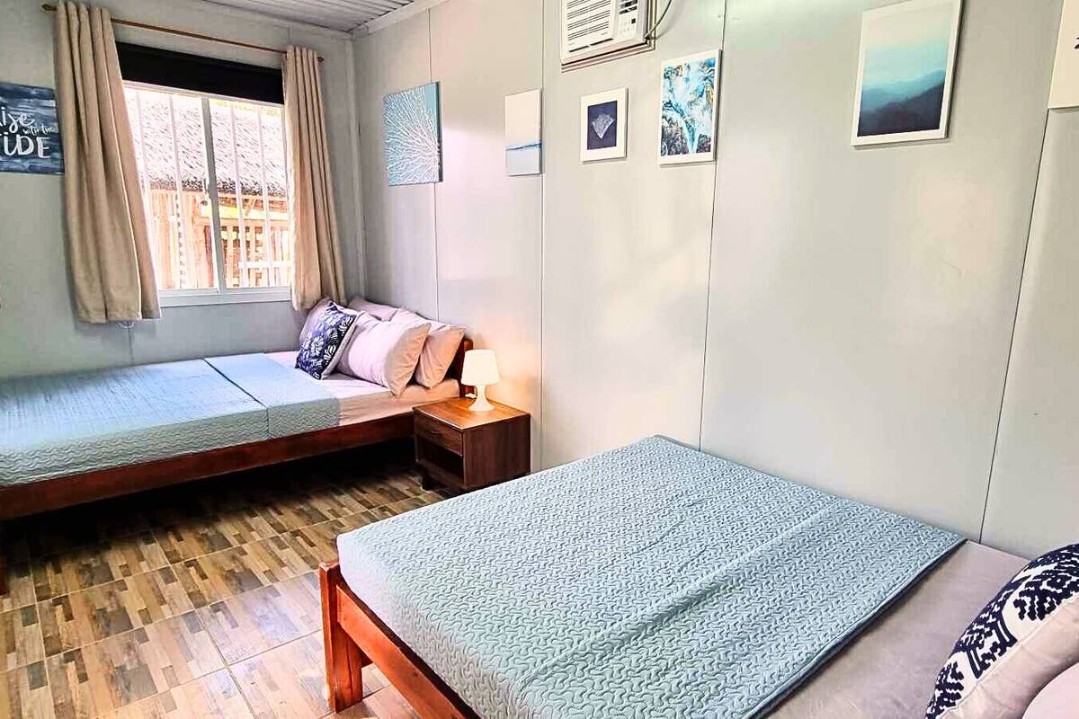 A bedroom with two single beds, a wooden floor, a window with curtains, and wall decorations.