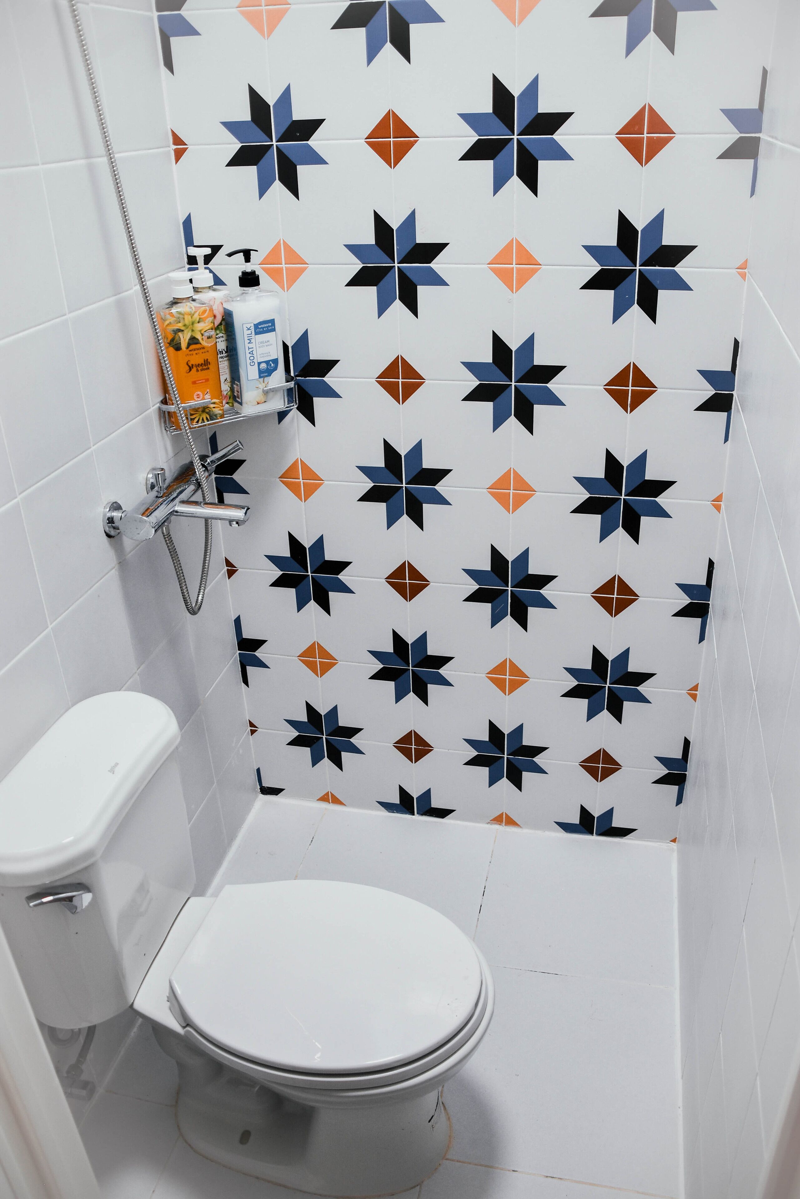 Une salle de bain comprenant des toilettes, une douche et un mur recouvert de carreaux formant un motif géométrique.