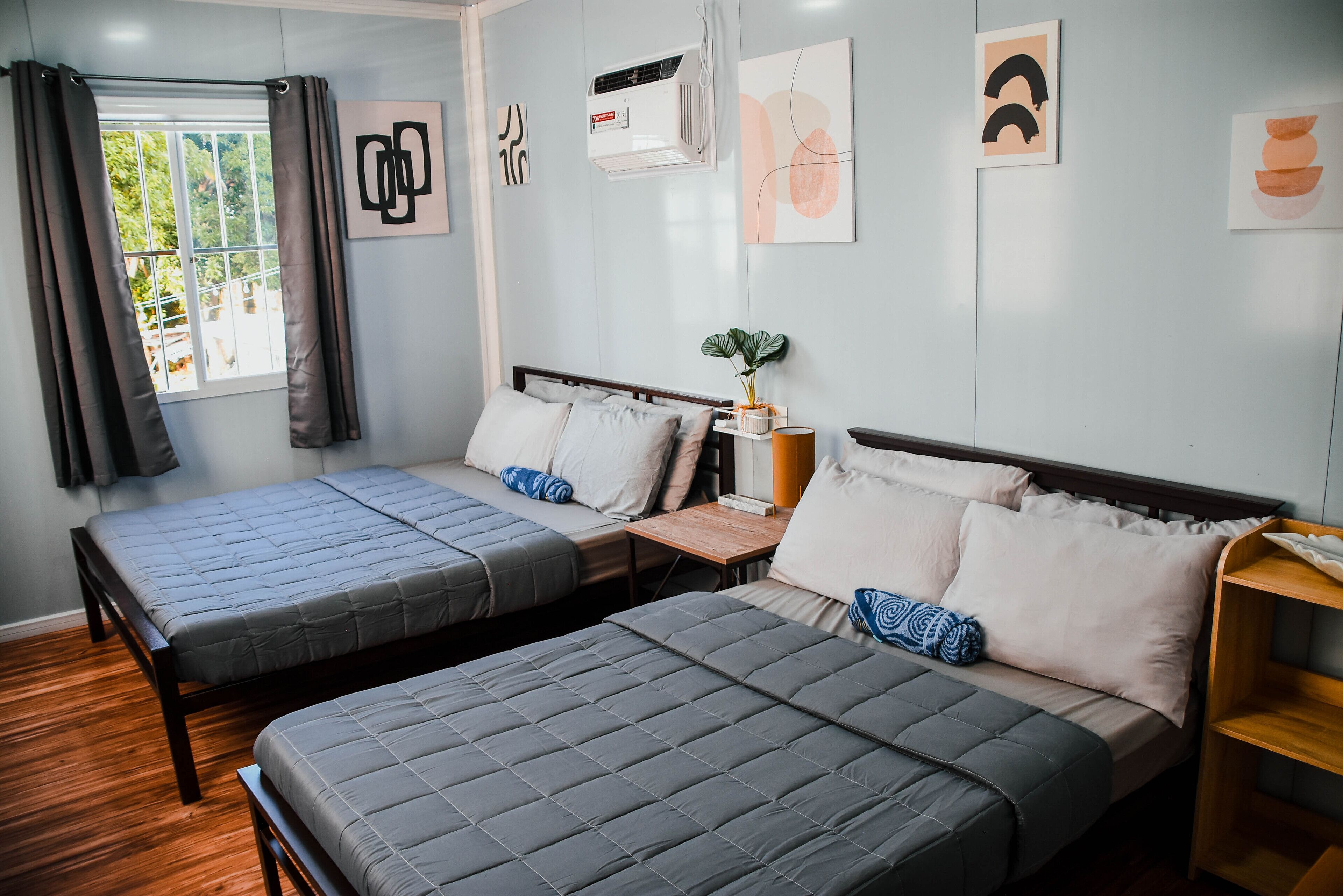 Ein Schlafzimmer mit zwei Betten, einem fenster mit Vorhängen, einer Klimaanlage und Wandbildern.