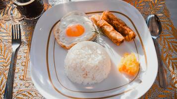 A plate with fried egg, rice, spring rolls, and orange slices on a table with a lace tablecloth.