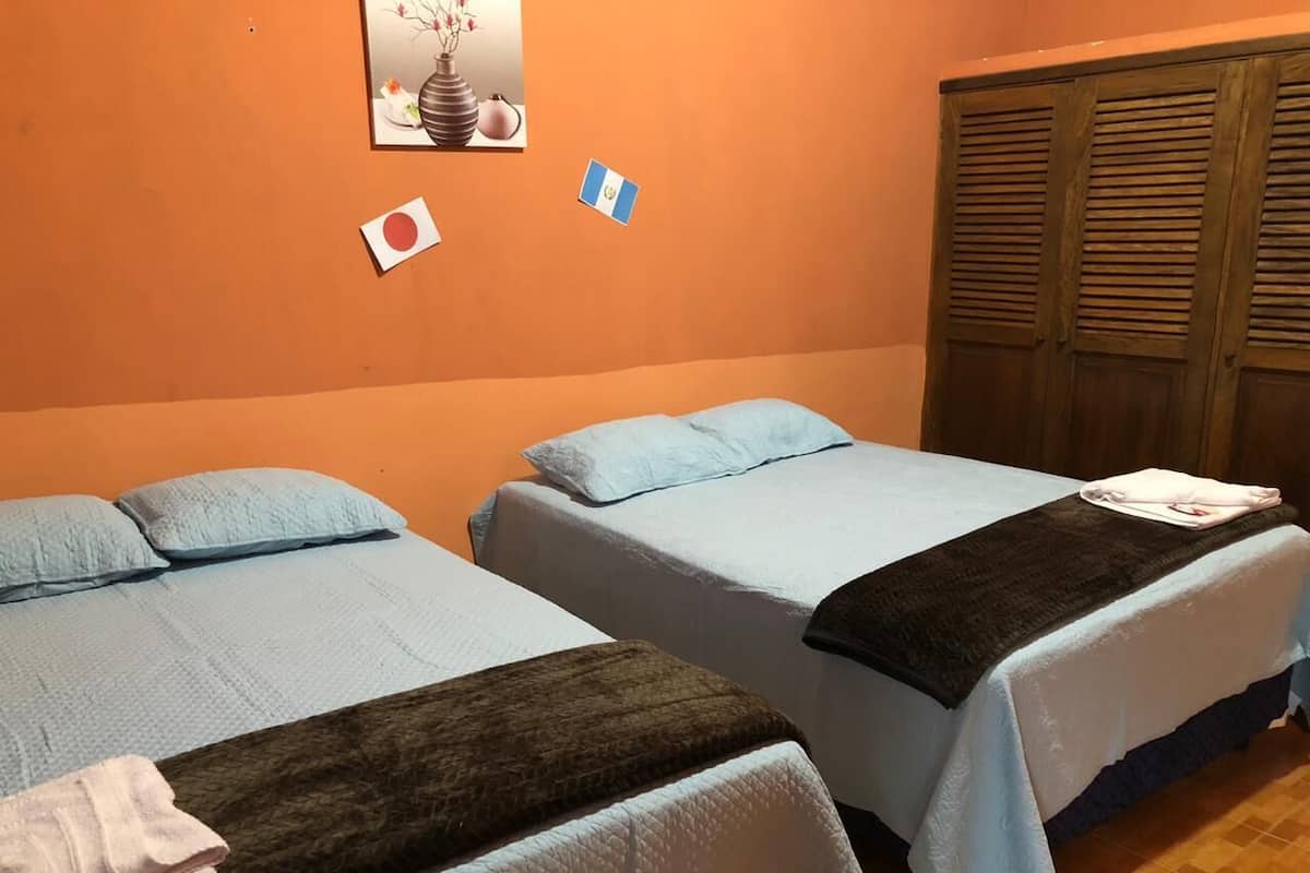 Une chambre avec deux lits, chacun recouvert d’une couvre-lit bleue et d’une couverture marron. Il y a des serviettes sur les lits. La chambre a un mur orange et une armoire en bois.