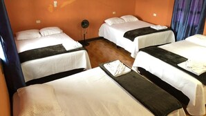 Ein Hotelzimmer mit vier Betten, die quadratisch angeordnet sind, einem kleinen Tisch in der Mitte und einem Wandventilator.