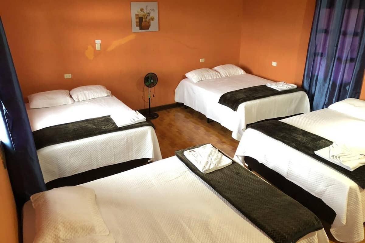 Une chambre d’hôtel avec quatre lits disposés en carré, une petite table au centre et un seul ventilateur fixé au mur.