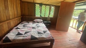 A wooden room with a bed, a small table, and a door leading outside. - CABAÑAS TAKANA (Leticia)