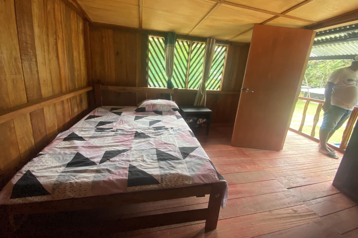 A wooden room with a bed, a small table, and a door leading outside.