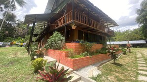 A two-story wooden house with a balcony, surrounded by lush greenery and palm trees. - CABAÑAS TAKANA (Leticia)