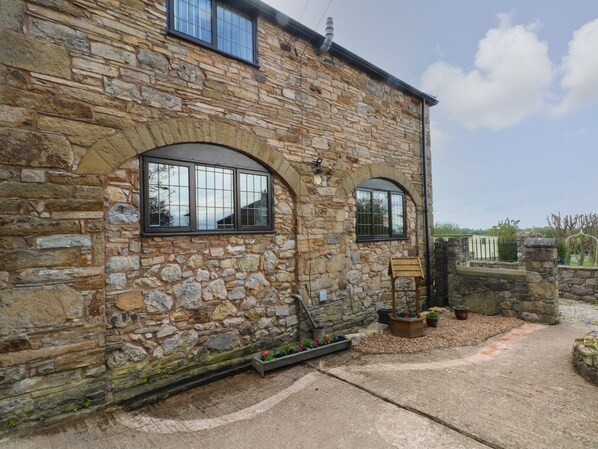 A stone building with two arched windows, a small wooden bench, and a garden area with potted plants. - The Coach House (Holywell)