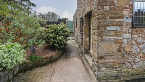 A narrow stone pathway leading to a stone building with a window. - The Coach House (Holywell)